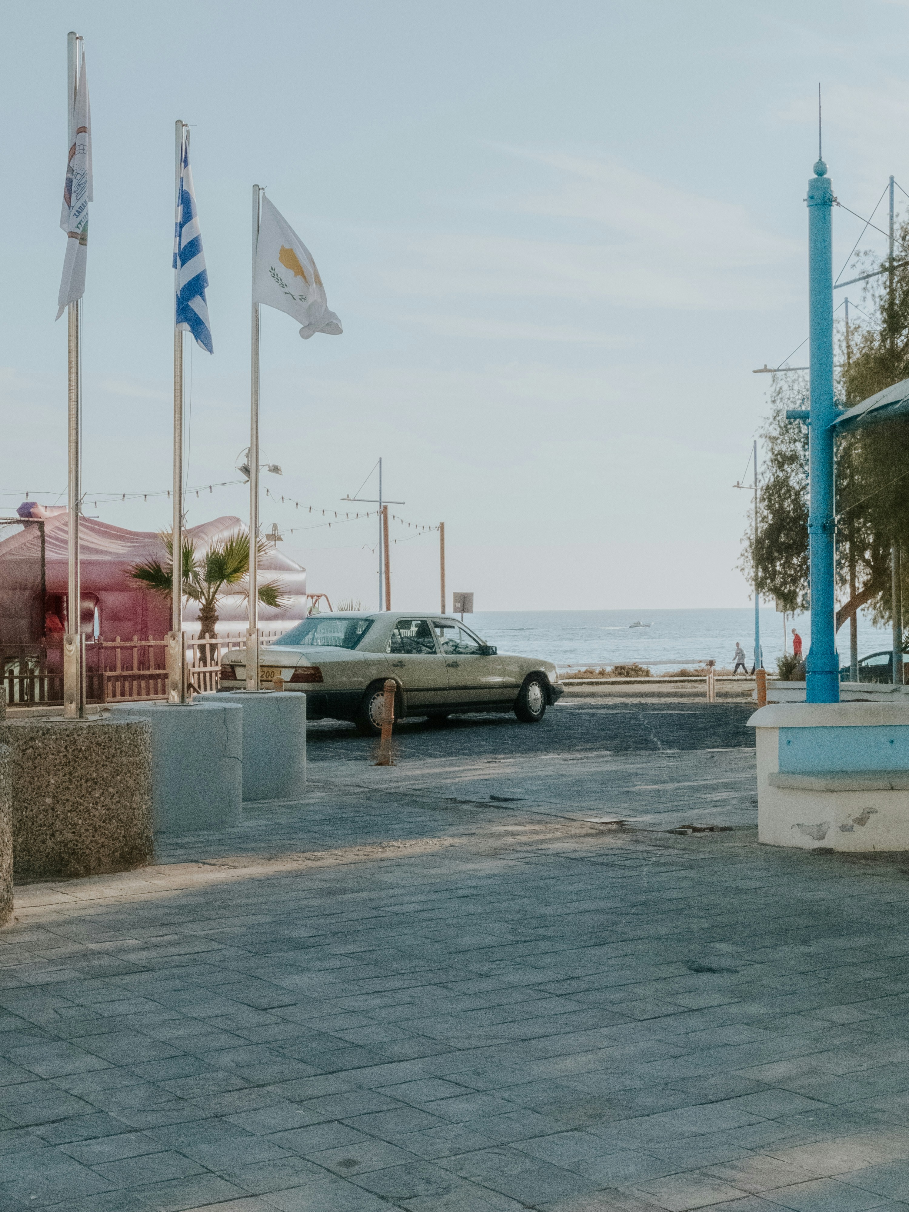 Coche aparcado junto al paseo marítimo, con el mar y banderas al fondo