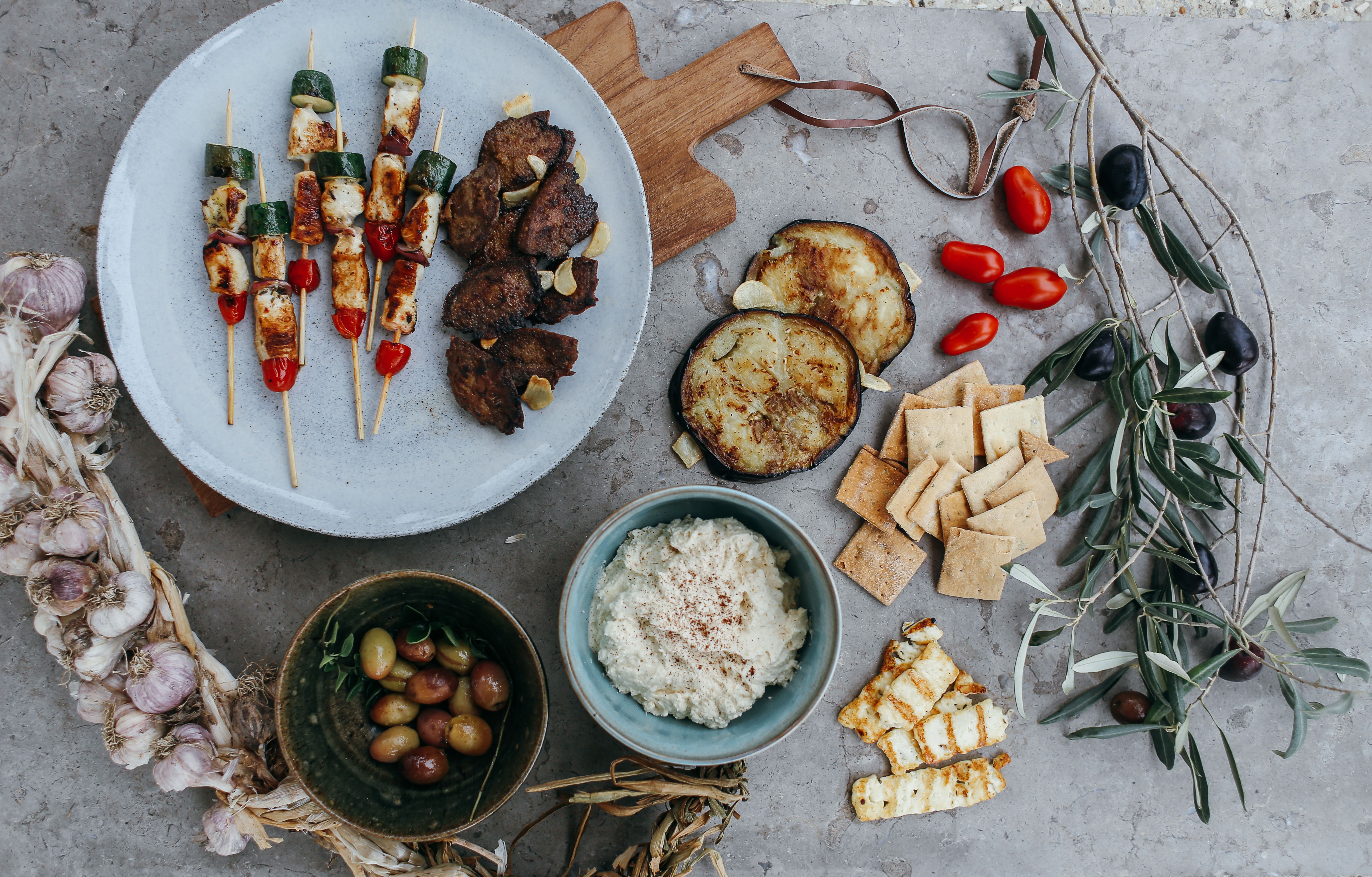 Mesa con brochetas de halloumi y verduras, carne, berenjena, aceitunas y una crema para compartir