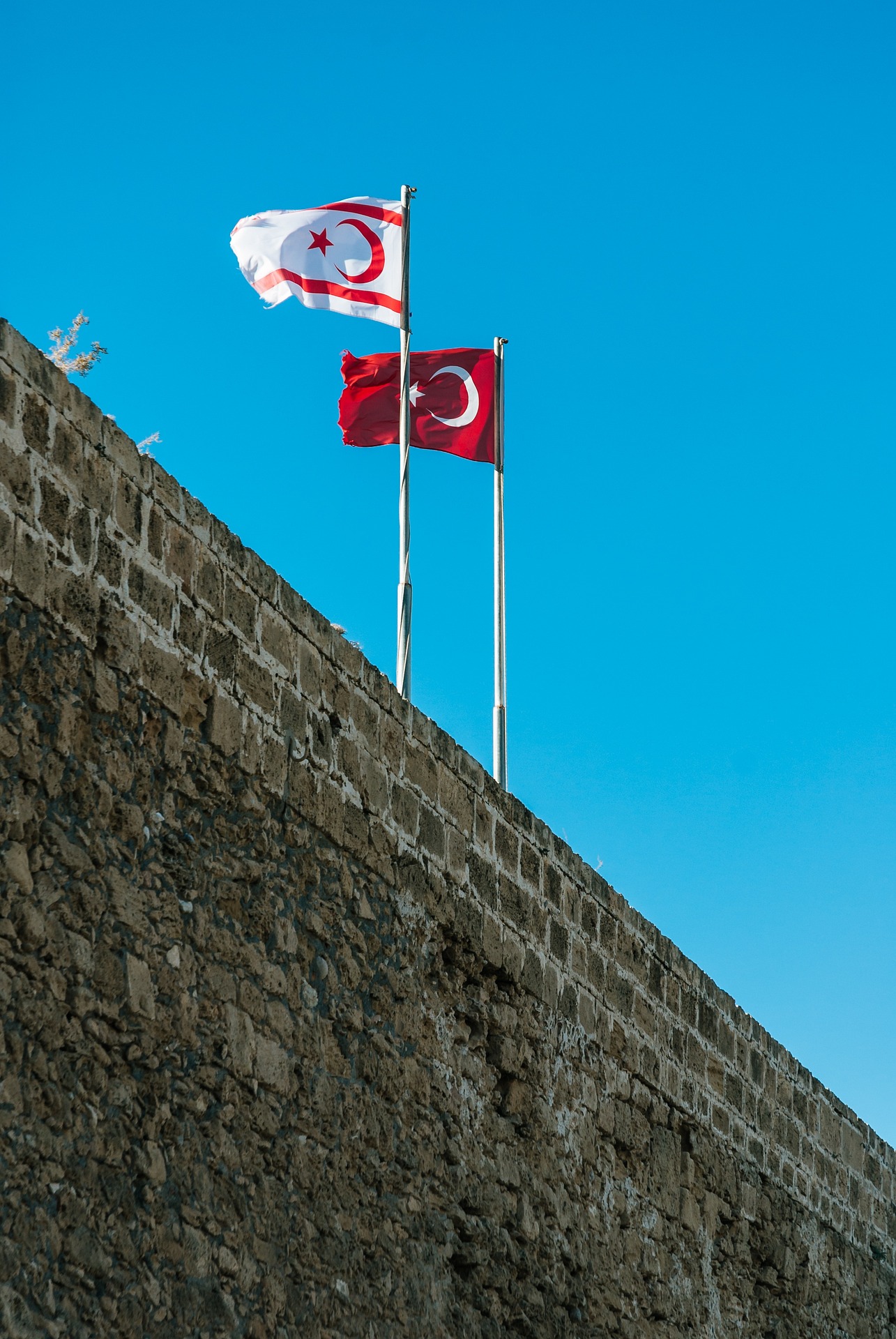 Banderas turcochipriota y turca sobre una muralla de piedra, con cielo azul